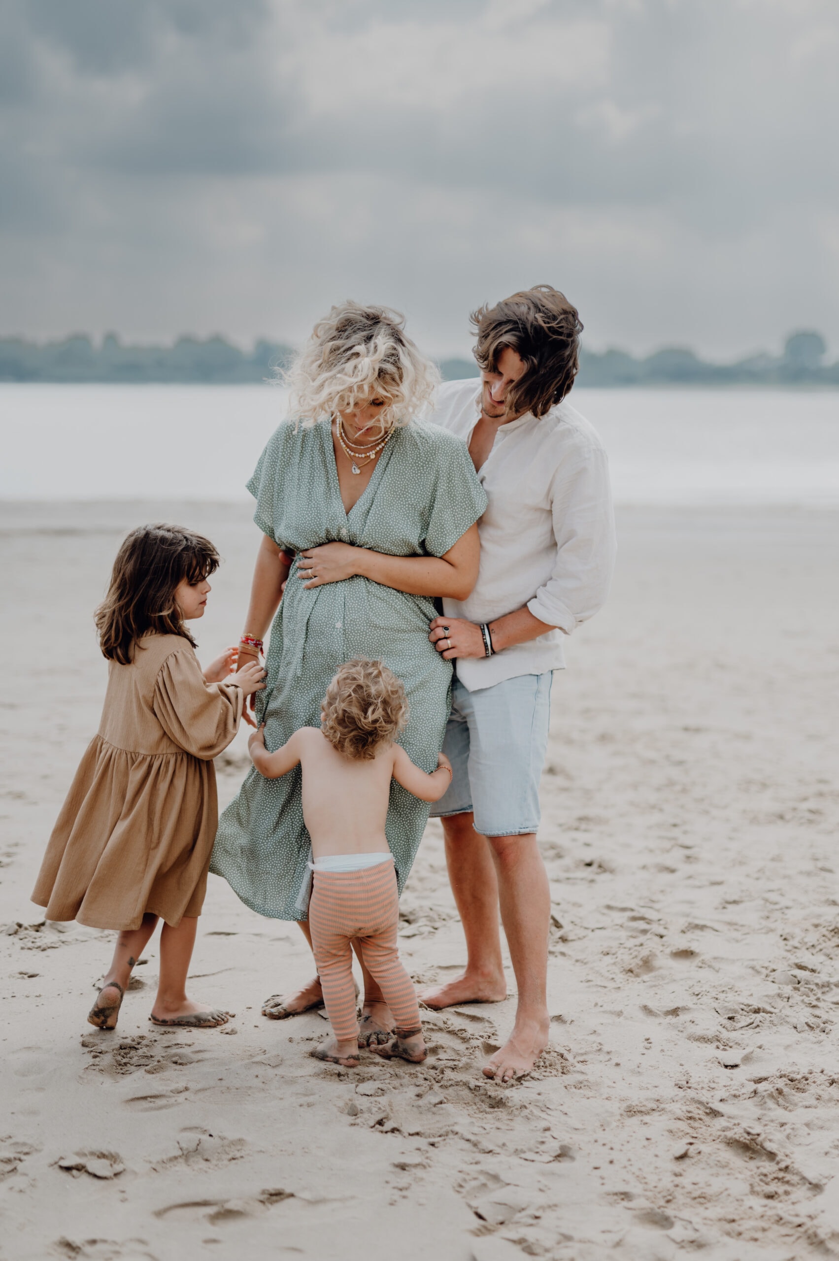 Eine Familie steht am Strand mit zwei Kindern und Babybauch